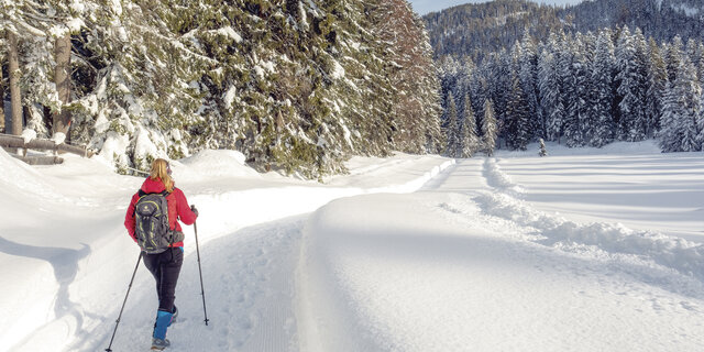 Ein Wanderer geht mit Wanderstöcken auf einem verschneitem Weg.