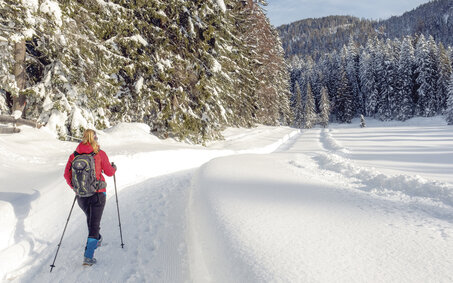 Ein Wanderer geht mit Wanderstöcken auf einem verschneitem Weg.