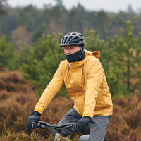 Mann mit gelber Jacke sitzt auf einem Fahrrad in herbstlicher Landschaft. Er hat eine Sturmhaube unter dem Helm und trägt Handschuhe.