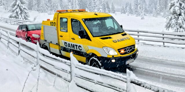 Ein ÖAMTC-Pannenfahrzeug schleppt in winterlicher Landschaft ein rotes Auto ab.
