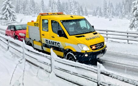 Ein ÖAMTC-Pannenfahrzeug schleppt in winterlicher Landschaft ein rotes Auto ab.