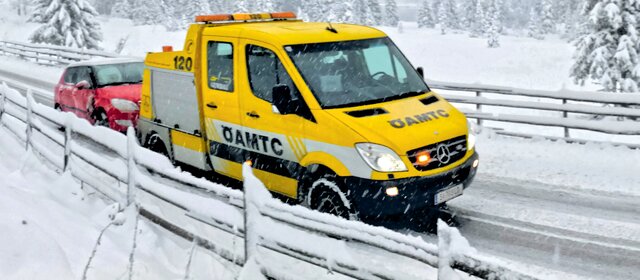 Ein ÖAMTC-Pannenfahrzeug schleppt in winterlicher Landschaft ein rotes Auto ab.