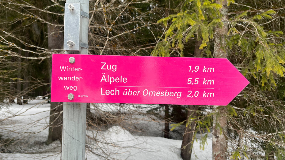 Eine pinke Tafel zur Orientierung, auf der verschiedene Winterwanderwege geschrieben stehen sowie die Distanz dieser Wege.