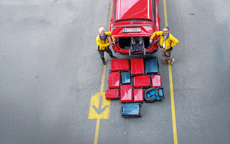 Heckansicht eines Autos von oben. Reisekoffer liegen vor dem Kofferraum.