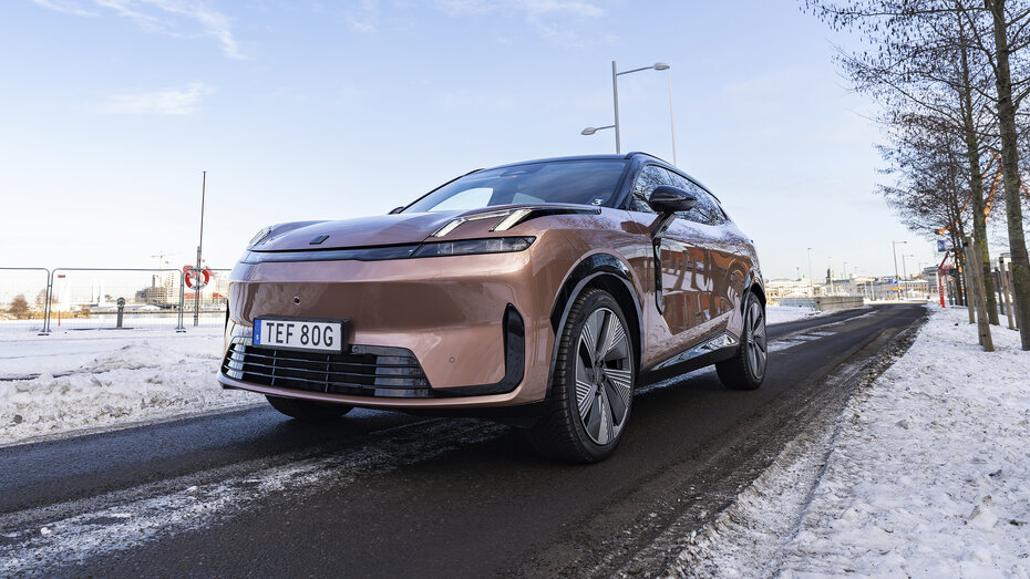 Ein kupferfarbener Lynk & Co 08 fährt auf einer Straße, neben der Schnee liegt.