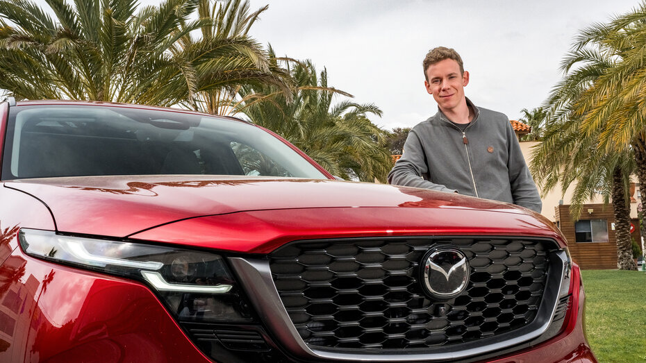 Ein Mann in grauer Weste lehnt an der Motorhaube eines roten Mazda CX-5