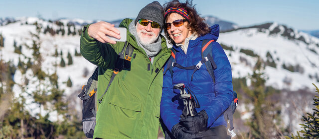 Senior couple hikers standing in snow-covered winter nature, taking selfie.