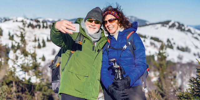 Senior couple hikers standing in snow-covered winter nature, taking selfie.