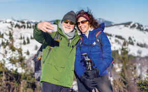 Senior couple hikers standing in snow-covered winter nature, taking selfie.