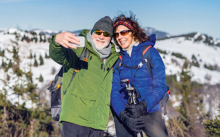 Senior couple hikers standing in snow-covered winter nature, taking selfie.