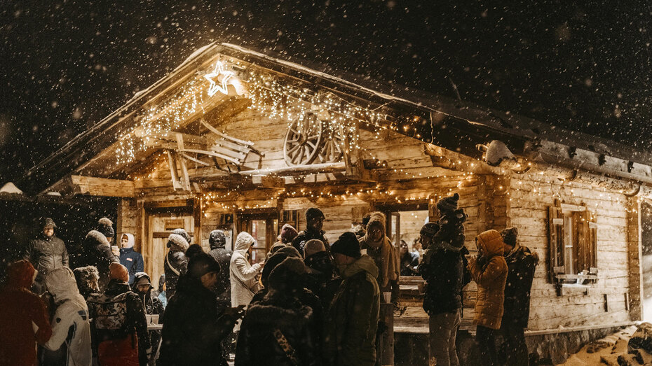 Beleuchtete Weihnachtsholzhütte in der Nacht. Viele Menschen stehen davor und trinken ein Heißgetränk.