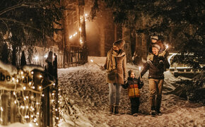Eltern gehen mit zwei Kindern im Schnee im Wald. Die Werg ist mit beleuchtet.