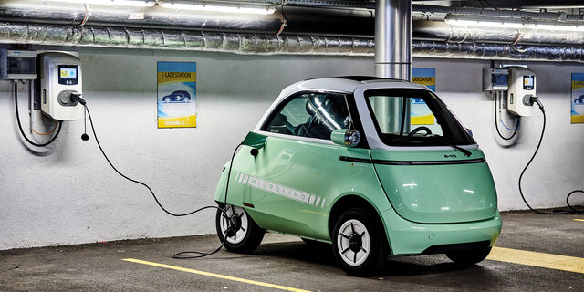 Das Kleinfahrzeug Microlino in hellgrün steht an einer Ladestation angesteckt in einer Garage.