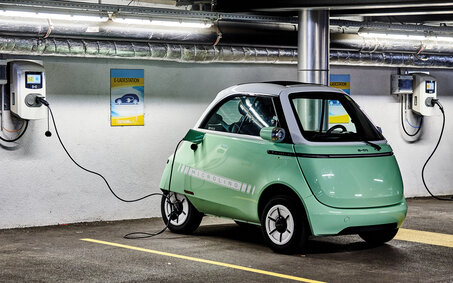 Das Kleinfahrzeug Microlino in hellgrün steht an einer Ladestation angesteckt in einer Garage.