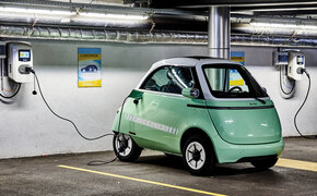 Das Kleinfahrzeug Microlino in hellgrün steht an einer Ladestation angesteckt in einer Garage.