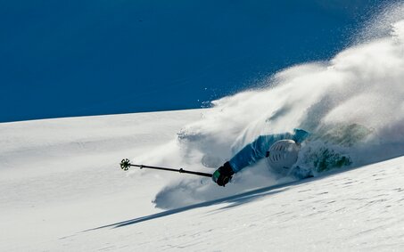 Skifahrer stürzt bei der Abfahrt auf einem verschneiten Berghang.