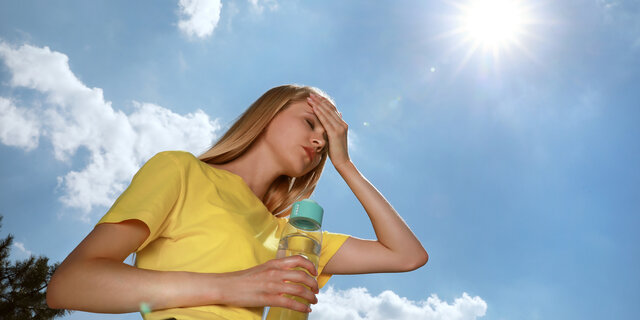 Frau mit Wasserflasche, die im Freien an einem Hitzeschlag leidet.