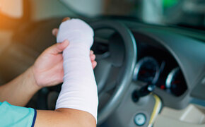 Ein verletzter Mann mit einem Verband an Hand und Arm fährt ein Auto, was zu einem Unfall führen könnte, weil es unbequem ist, wie mit einer normalen Hand zu fahren.