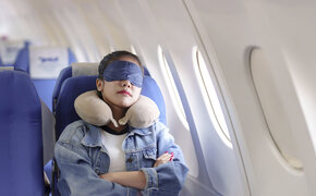 Frau schläft mit Schlafmaske in Flugzeug.