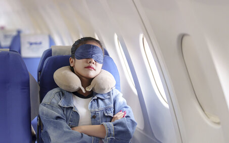 Frau schläft mit Schlafmaske in Flugzeug.