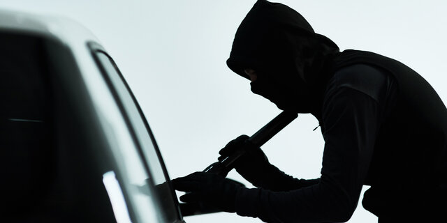 Silhouette eines vemummten Mannes, der ein Auto knackt