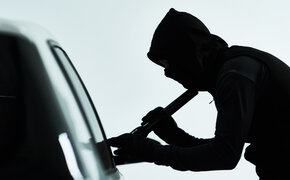Silhouette eines vemummten Mannes, der ein Auto knackt