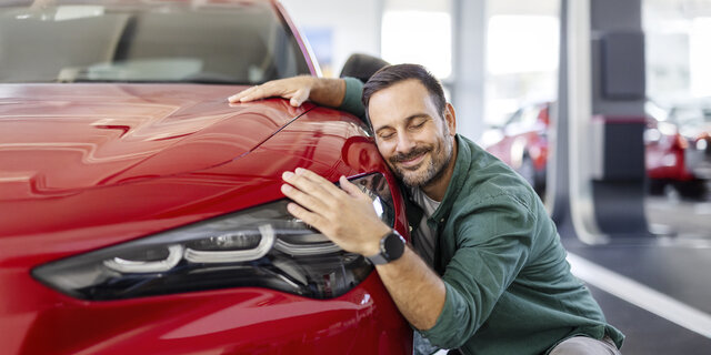 Ein Mann kuschelt lächelnd mit einem roten Auto