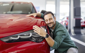 Ein Mann kuschelt lächelnd mit einem roten Auto
