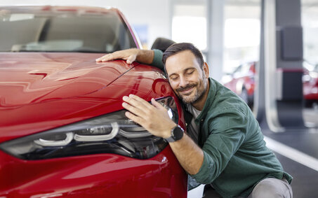 Ein Mann kuschelt lächelnd mit einem roten Auto