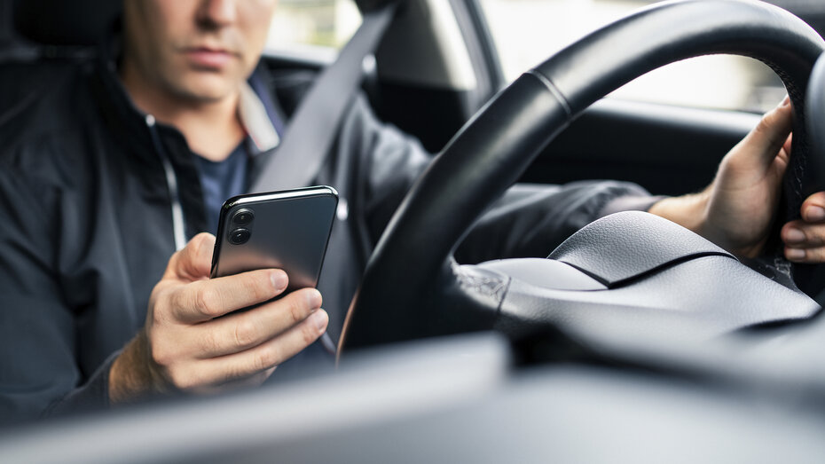 Ein Mann hat am Steuer sein Handy in der Hand