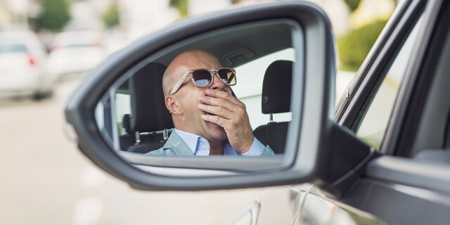 Mann mit Sonnenbrille sitzt gähnend im Auto.