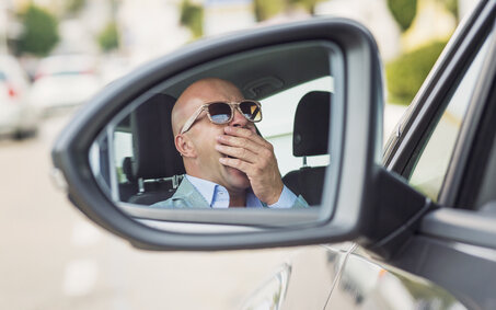 Mann mit Sonnenbrille sitzt gähnend im Auto.