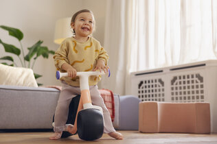 Imagebild des neuen Woom Wow Laufrads. Kind lacht und sitzt am Laufrad im Kinderzimmer.