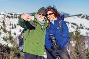 Senior couple hikers standing in snow-covered winter nature, taking selfie.