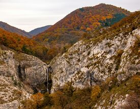 Blick auf mit herbstlichen Laubbäumen bedeckte Berge und einen Wasserfall