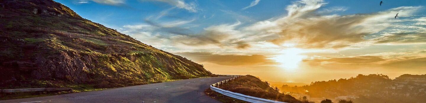Eine Straße schlängelt sich um einen Hügel, mit einem Sonnenuntergang im Hintergrund.