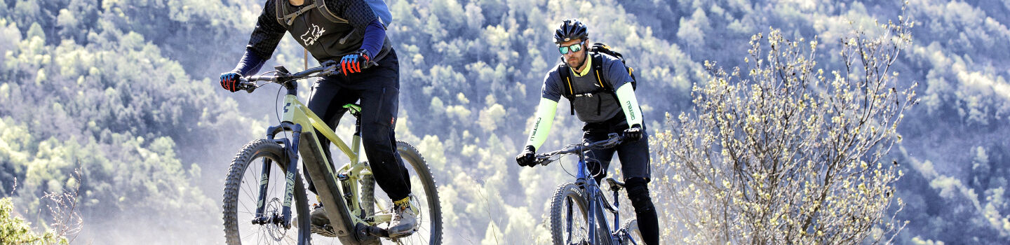 2 Radfahrer auf E-Mountain-Bikes unterwegs auf einem Berg.