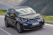BMW i3 E-Auto in dunkelblau fährt auf einer Straße, im Hintergrund Wiese und Berge.
