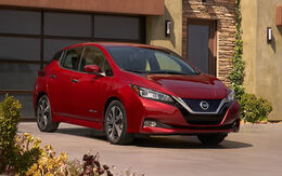 Roter Nissan Leaf steht vor einer Garage, im Vordergrund sind Blumen sichtbar.