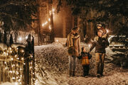 Eltern gehen mit zwei Kindern im Schnee im Wald. Die Werg ist mit beleuchtet.