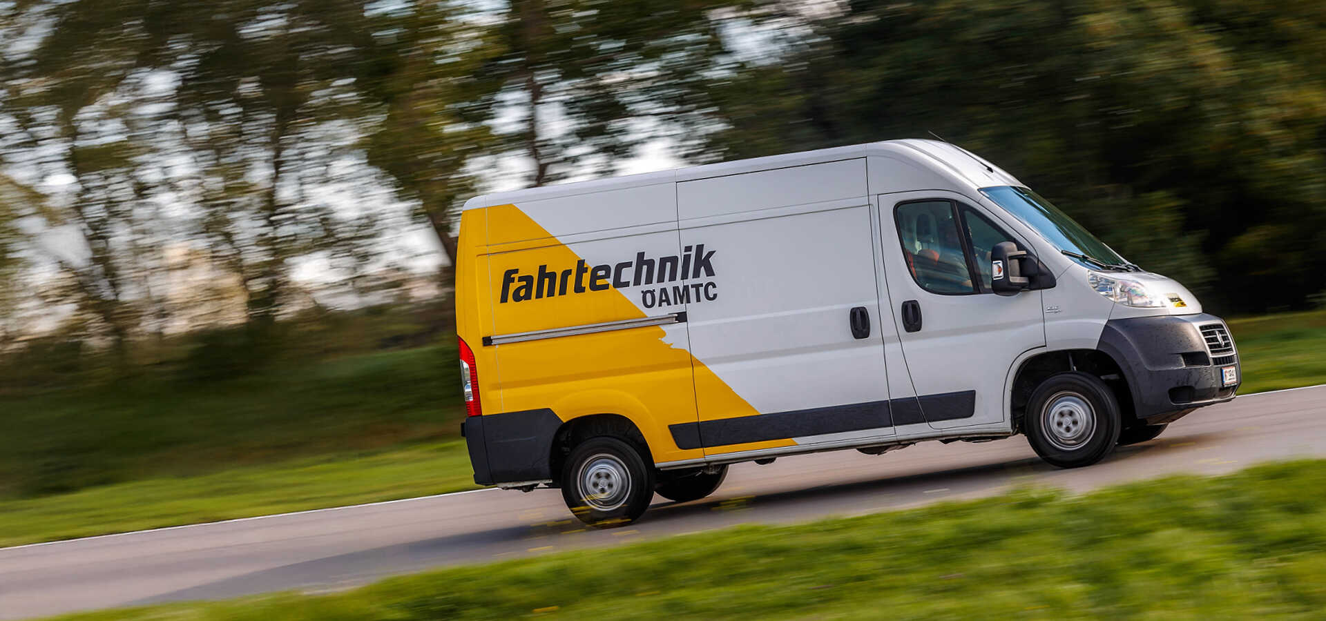 Weiß-Gelber Transporter mit ÖAMTC Fahrtechnik Logo auf einer Straße