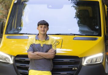 Auf dem Bild sieht man einen jungen ÖAMTC Mitarbeiter. er lehnt mit verschränkten Armen an einen gelben Klein LKW.