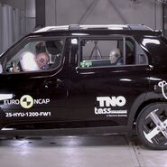 Das Foto zeigt ein schwarzes Auto von der Seite, das gerade im Zuge eines Crashtests frontal gegen ein Hindernis prallt.