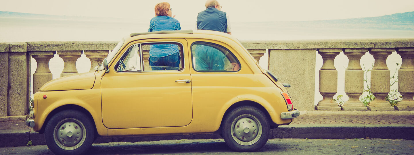 Ein Fiat 500 Oldtimer steht auf einer Brücke, während zwei Personen die Aussicht genießen.