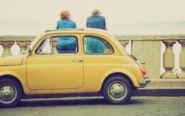 Ein Fiat 500 Oldtimer steht auf einer Brücke, während zwei Personen die Aussicht genießen.