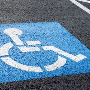 Behindertenparkplatz mit einem blau/weißen Rollstuhlpiktogramm auf Straßenasphalt.