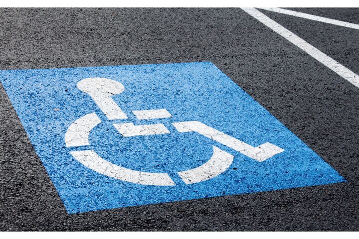 Behindertenparkplatz mit einem blau/weißen Rollstuhlpiktogramm auf Straßenasphalt.