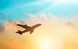 Ein Flugzeug fliegt vor einem farbenfrohen Sonnenuntergangshimmel mit Wolken.