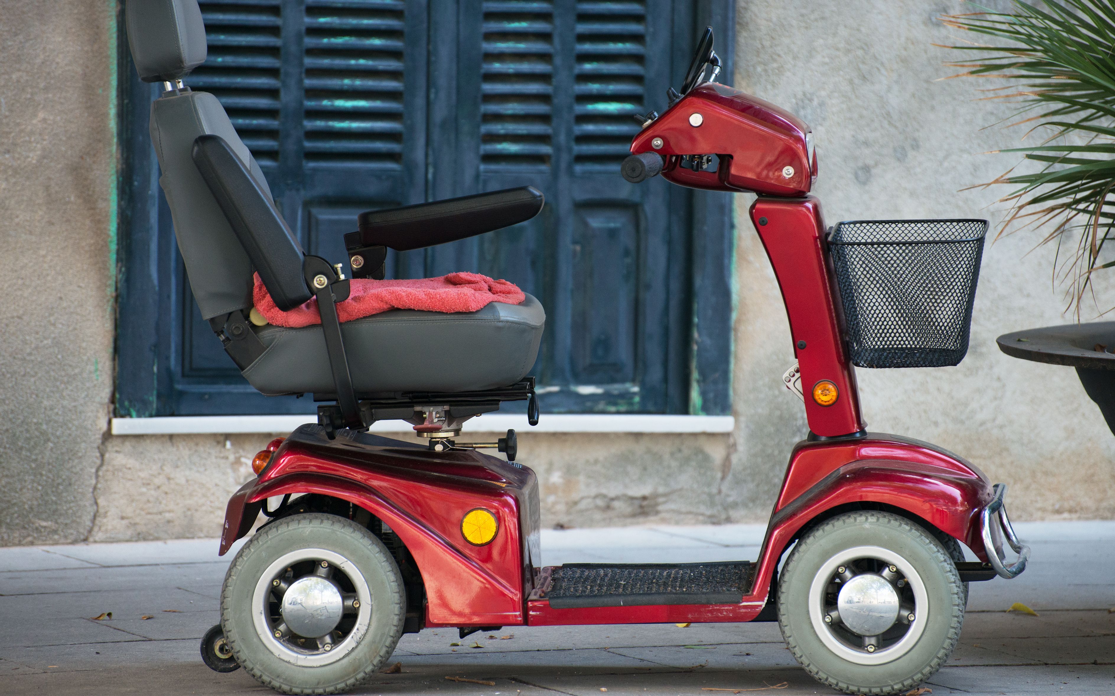 Elektro-Seniorenmobil: Motorisierter Rollstull  in der Farbe Rot für Menschen mit Behinderungen steht vor Gebäude.