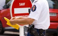 Ein Polizist, der ein gelbes Dokument oder Formular in der Hand hält. Im Hintergurnd ist ein rotes Verbotsschild mit einem weißen Balken und der Aufschrift "SAUF AUTORISATION" zu sehen. Ein rotes Auto ist ebenfalls im Hintergrund zu erkennen.
